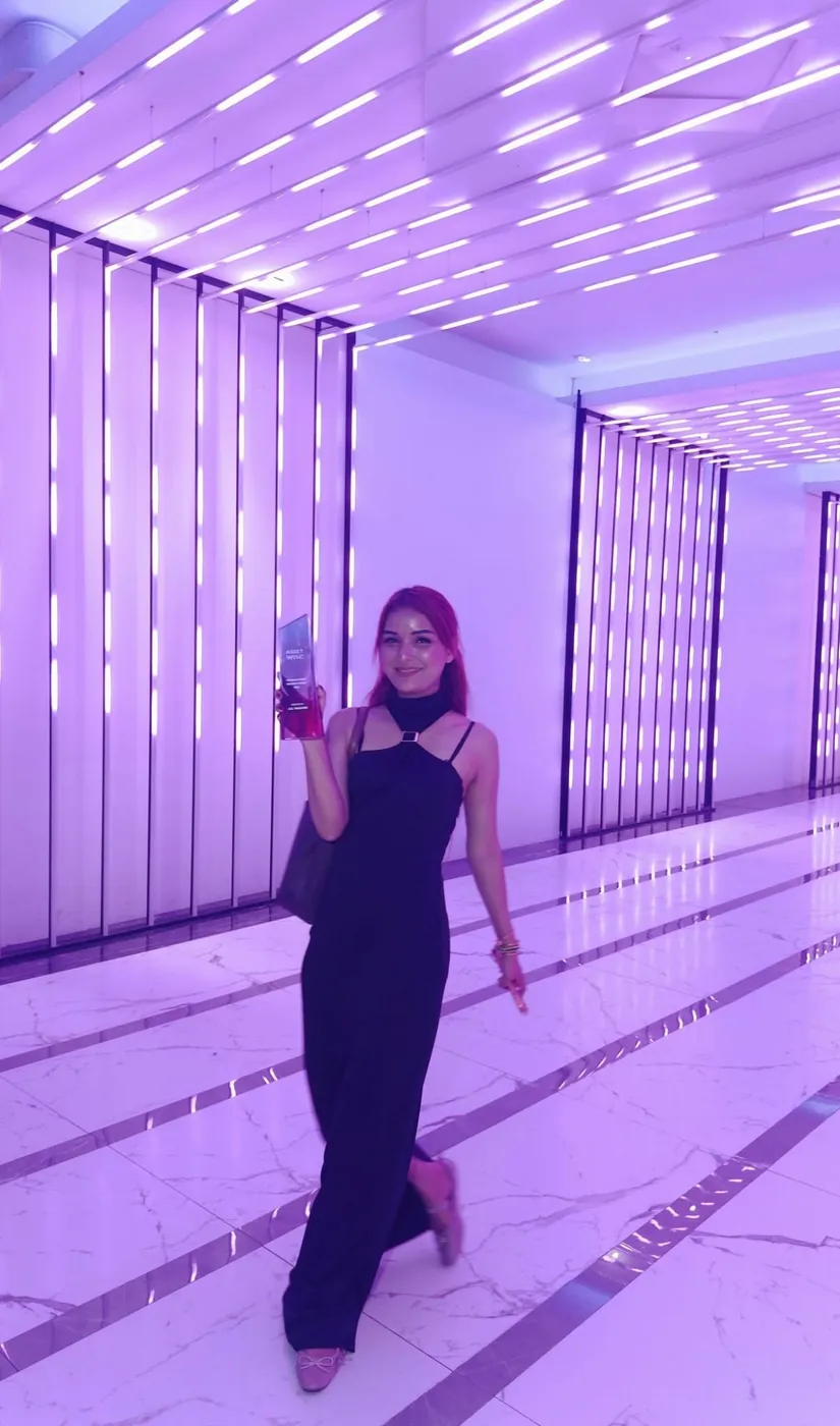 An A.D. advisor holding her award in a corridor lit in violet