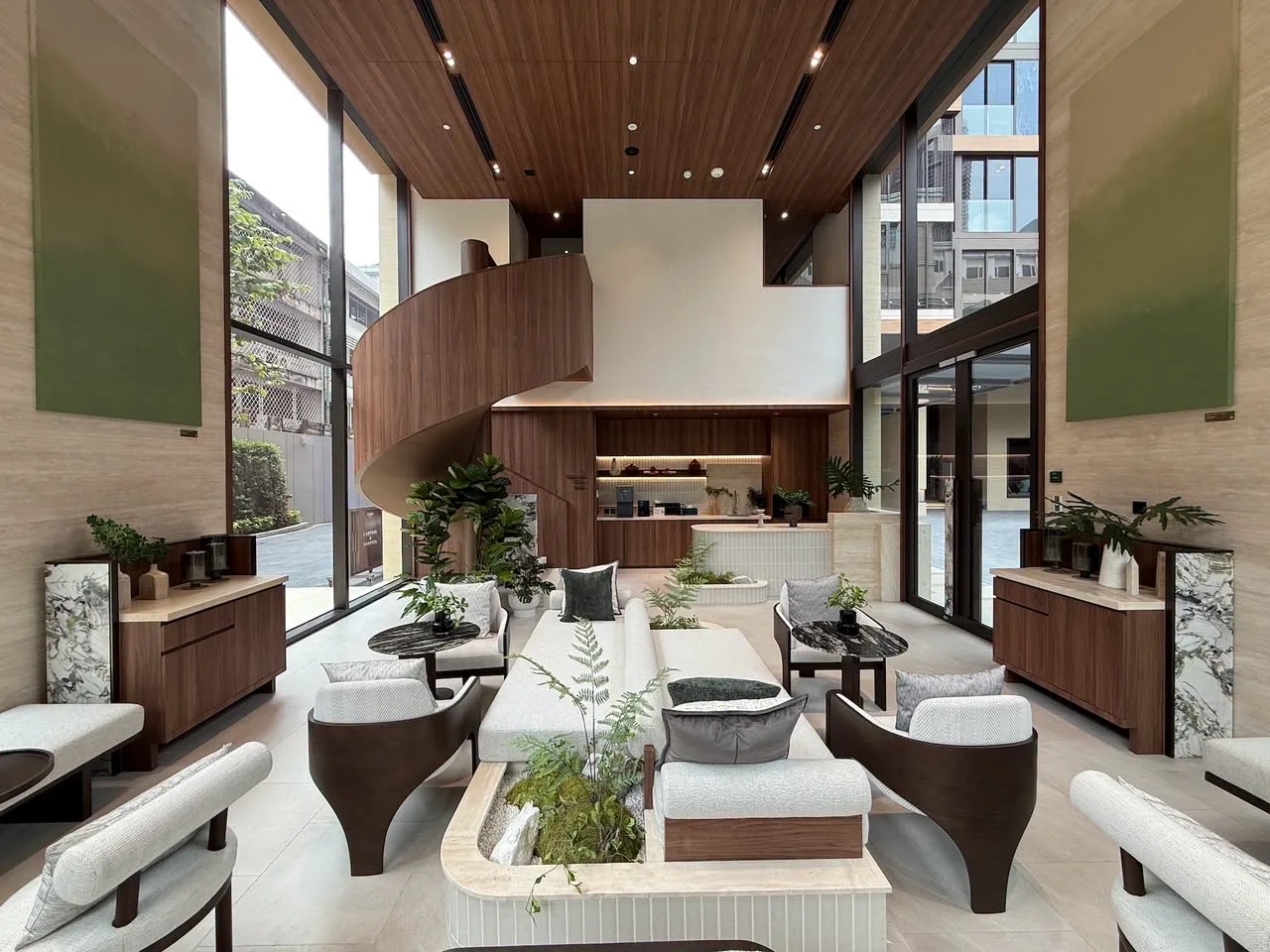 A double-height lounge with a timber spiral staircase, cream sofas and green marble